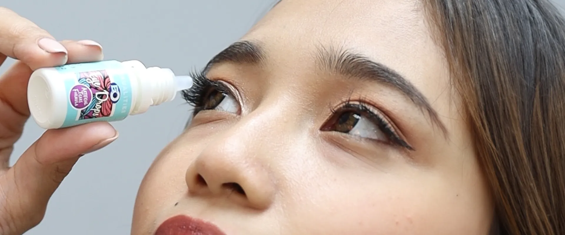 A woman putting eye drops on her right eye.